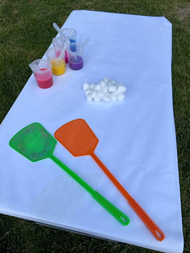 table covered in white paper with cotton balls, fly swatters, paint cups, and pipettes.