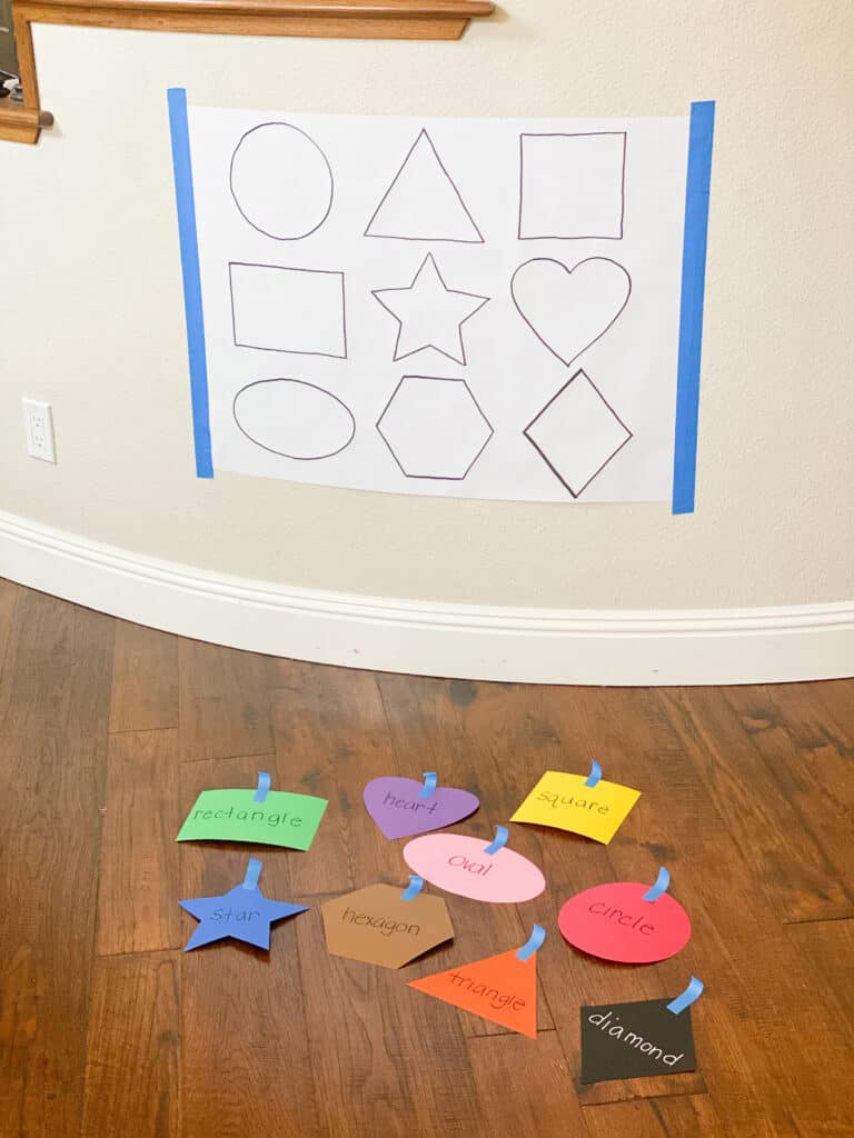 black and white paper with shapes on it and colored shape cut outs on the floor