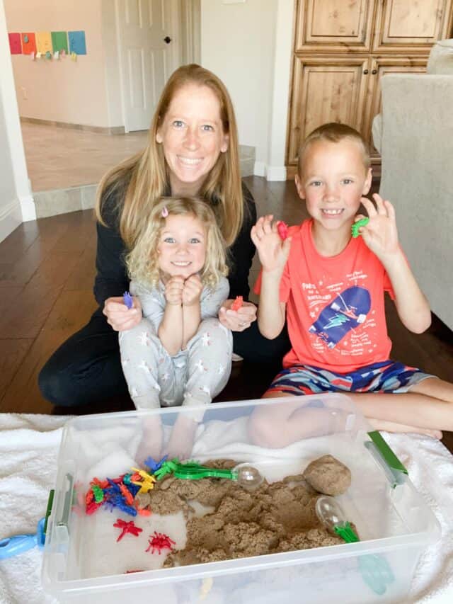 mom and three kids with a plastic tub of kinetic sand