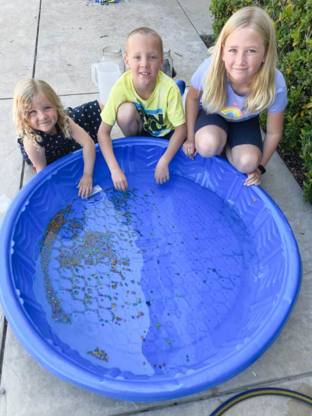 three kids sitting by a baby pool with water beads