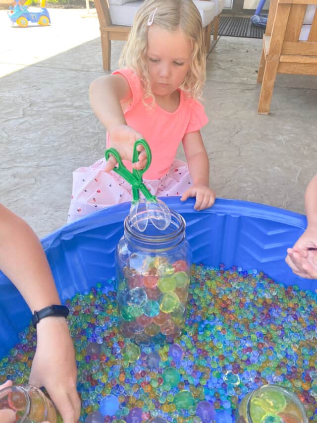 little girl using a scissor scoop with water beads